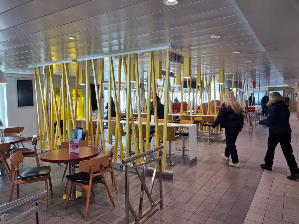 Sitzgruppen zwischen gelben Säulen im Cafeteria-Bereich der Fähre Berlin