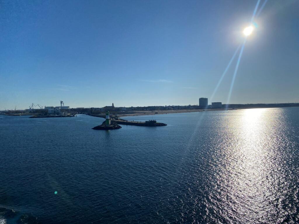 Groen havenlicht op de westelijke pier van Warnemünde met vuurtoren en strand, gezien vanaf de veerboot