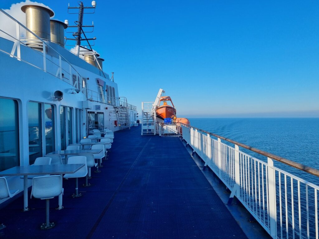 Outdoor seating along the promenade deck of the Berlin ferry with lifeboats and open sea ahead